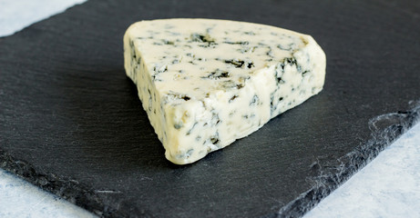 Stilton blue mold cheese wedge close up on black slate cheese board with selective focus