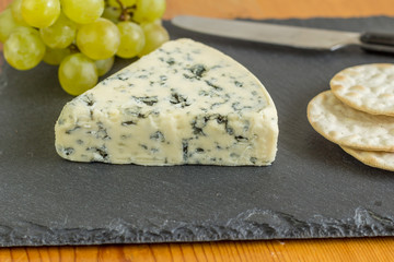 Stilton blue mold cheese wedge close up on black slate cheese board with selective focus