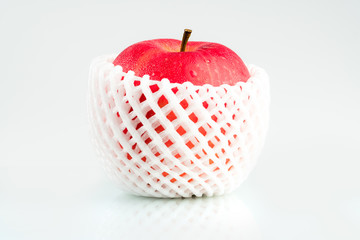 A red apple with water drops on skin in white shockproof foam net wrap isolated on white background...