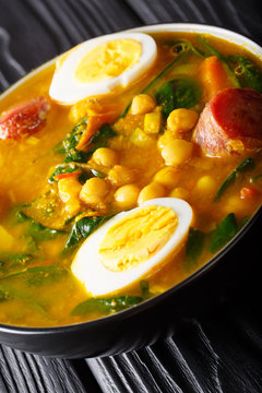 Spanish stew spinach with chickpeas, sausages and eggs close-up in a bowl. vertical