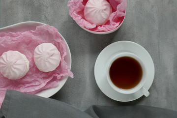 morning coffee in gray pink tones. cup with coffee and pink marshmallow in a  oval dish on a gray background.  flat lay , top view,copy space