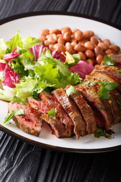 Grilled Carne Asada steak with salad and beans close-up on a plate. vertical