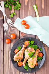 Baked chicken legs in spices with tomatoes and greens in a plate on a wooden table. Top view