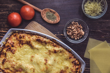 lasagne layered served on a wooden board with fresh tomatoes alongside