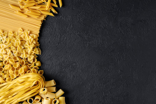 Raw Italian pasta fettuccine, paccheri, farfalle, spaghetti, penne, conchiglie on a dark background.