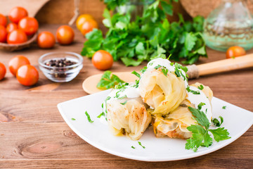 Appetizing ready-to-eat cabbage rolls with minced meat, sour cream and fresh herbs on a plate on a wooden table