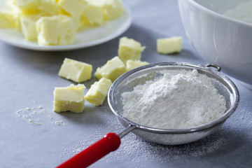 Wheat flour on a sieve and diced butter on a table top in the kitchen being prepared as ingredients for baking some cake or bread.