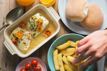 Table with baked cod cherry tomato, chips, red cherry tomatoes, buns and orange drink