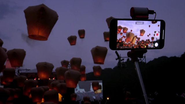 4K Tourist people using smart phone for take pictures of launching many asian fire lanterns during buddhist festival in chinese new year. Rice paper hot air balloons in sky lantern celebration-Dan