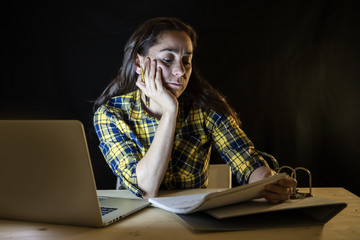 Overworked and tired student woman studying late at night on black background.