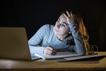 Overworked and tired student woman studying late at night on black background.