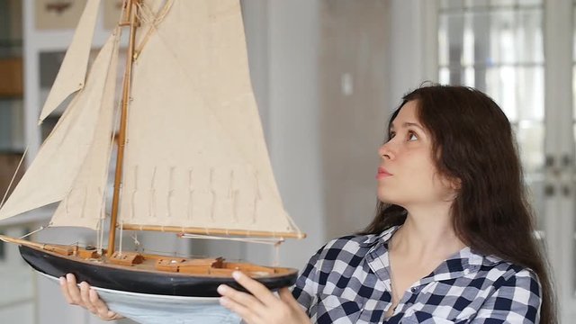 A happy young woman is holding a model of a sailing ship