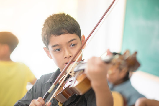 Little boys play and practice violin in the music class room