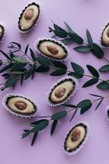 Composition of delicious praline sweets with almonds and green twigs on purple background