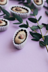 Composition of delicious praline sweets with almonds and green twigs on purple background