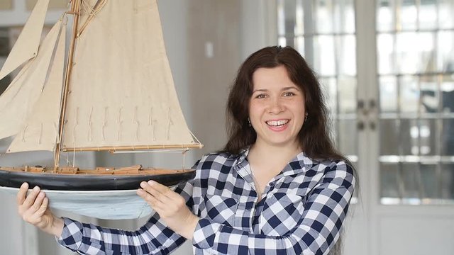 A happy young woman is holding a model of a sailing ship