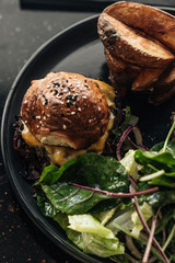 Delicious burgers with lettuce on black plate in cafe
