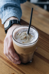 Male hand holding glass of delicious cappuccino coffee on wooden table
