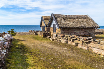 Two limestone fishing cabins with thatched roofs at the old Bruddesta fishing village on Oland, Sweden. Horizon over Baltic sea in the background.