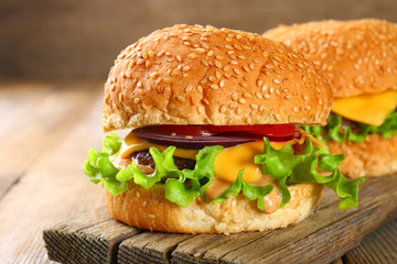 Tasty homemade burger consisting of bun, patties, salad, red onion and tomato on an old wooden table.