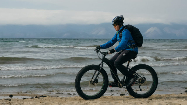 Fat bike also called fatbike or fat-tire bike in summer driving on the beach. The guy is going straight on the beach. On the sand on such a bike ride is not difficult.