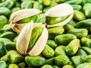 Green pistachio nut with shell over lot of pistachios.