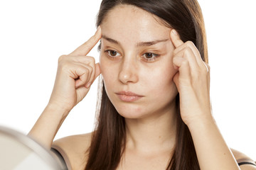 a young woman tightens her face with her fingers on a white background