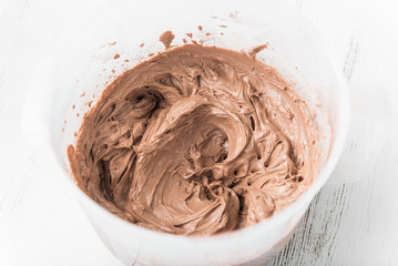 Cream cream for the cake: beaten butter with sugar, vanilla and cocoa powder in a whisk can on a white wooden table