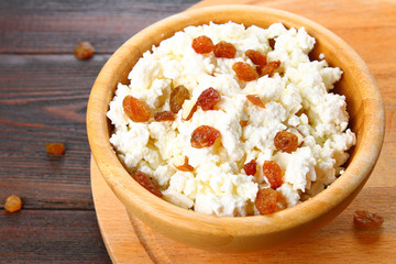 Homemade cottage cheese with almonds and raisins in a bowl on a wooden table.