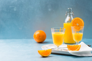 Glass of fresh orange juice with orange slices on white plate, blue background, cold summer refreshing nutritional beverage, blue orange color contrast, vitamin C healthy drink, copy space