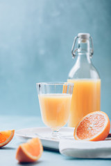 Glass of fresh orange juice with orange slices on white plate, blue background, cold summer refreshing nutritional beverage, blue orange color contrast, vitamin C healthy drink, copy space