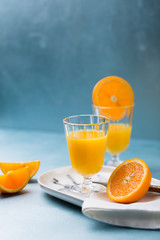 Glass of fresh orange juice with orange slices on white plate, blue background, cold summer refreshing nutritional beverage, blue orange color contrast, vitamin C healthy drink, copy space