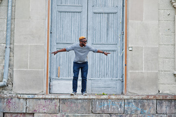 Stylish african american boy on gray sweater and black sunglasses posed on street. Fashionable black guy jump.
