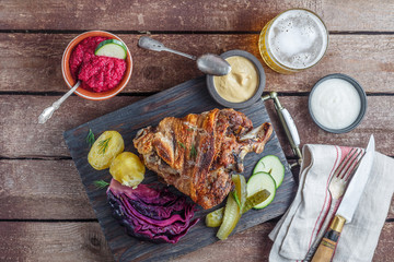 Roasted pork knuckle on black wooden board with appetizer and beer, copy space