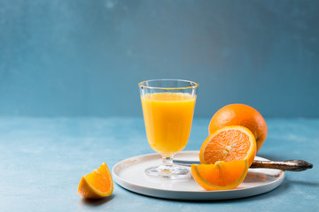 Glass of fresh orange juice with orange slices on white plate, blue background, cold summer refreshing nutritional beverage, blue orange color contrast, vitamin C healthy drink, copy space