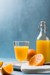 Glass of fresh orange juice with orange slices on white plate, blue background, cold summer refreshing nutritional beverage, blue orange color contrast, vitamin C healthy drink, copy space