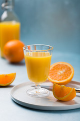 Glass of fresh orange juice with orange slices on white plate, blue background, cold summer refreshing nutritional beverage, blue orange color contrast, vitamin C healthy drink, copy space