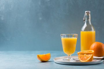 Glass of fresh orange juice with orange slices on white plate, blue background, cold summer refreshing nutritional beverage, blue orange color contrast, vitamin C healthy drink, copy space