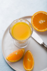 Glass of fresh orange juice with orange slices on white plate, blue background, cold summer refreshing nutritional beverage, blue orange color contrast, vitamin C healthy drink, copy space