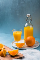 Glass of fresh orange juice with orange slices on white plate, blue background, cold summer refreshing nutritional beverage, blue orange color contrast, vitamin C healthy drink, copy space