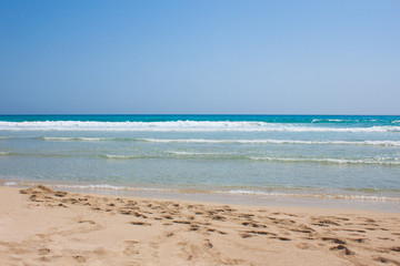 Fototapeta premium Blue sea with white waves and sand with footprints