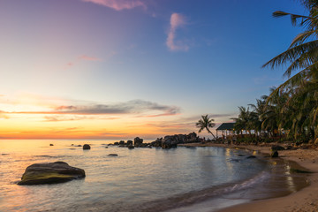 Fototapeta na wymiar Scenic colorful sunset on Phu Quoc Island Long Beach in Vietnam. Seascape on sandy coast with palm trees and stones in water