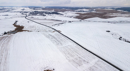 View from the air on the winter road in the field on which cars are going
