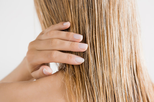 Young Woman With Hand Touching Her Wet, Blonde, Perfect Hair After Shower On The Gray Background. Care About Beautiful, Healthy And Clean Hair. Beauty Salon Concept. Back View.