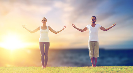 fitness and people concept - couple making yoga exercises outdoors over sea background