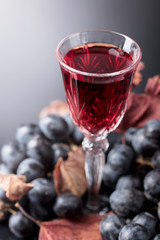 Crystal glass of red wine and grapes with dried vine leaves.