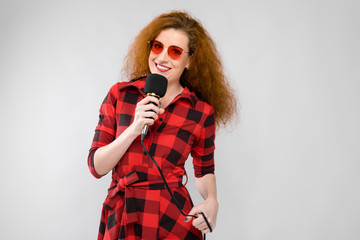 Portrait of beautiful redhead happy young woman in sunglasses smiling holding microphone on gray background