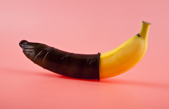 Banana with a black condom on a pink background. Safe sex concept