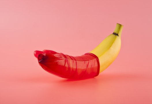 Banana with a red condom on a pink background. Safe sex concept