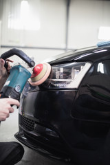 Fototapeta na wymiar Car detailing - Hands with orbital polisher in auto repair shop. Selective focus.
